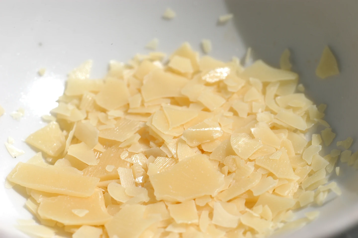 Flocos amarelos claros de cera de carnaúba em recipiente branco